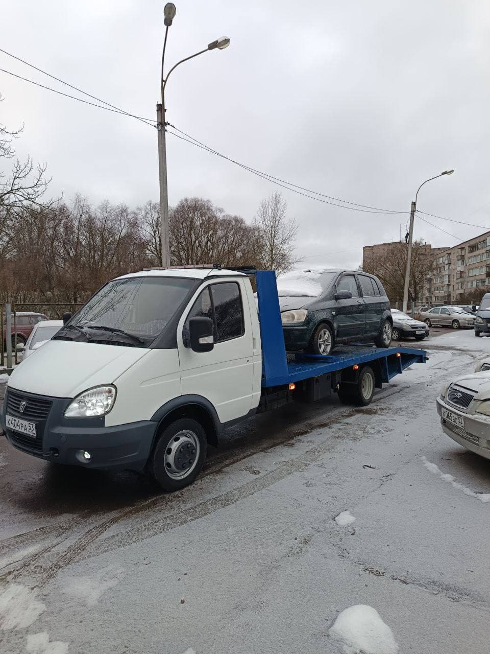 Эвакуатор с хэтчбеком на платформе зимой в Великом Новгороде